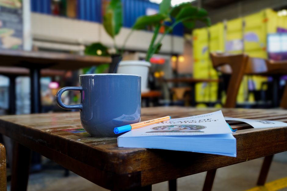 A serene setup with a blue mug and a book on a wooden table at a café in Houston, TX.